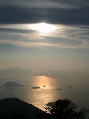 Sun, hidden behind clouds, setting over Hong Kong bay